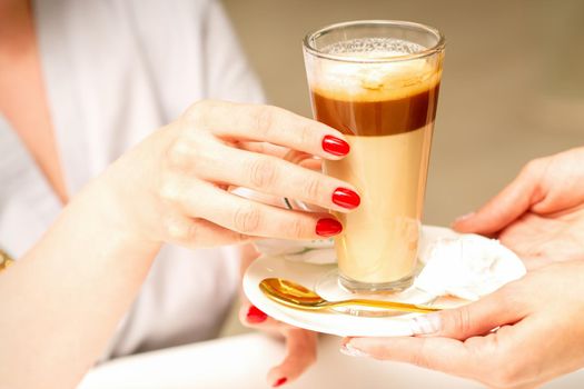 Barista serving coffee latte in glass mug for a customer, close up hands