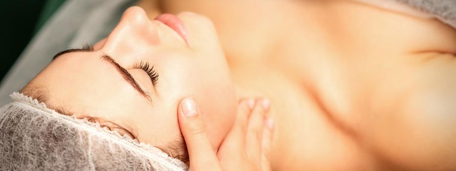 Facial massage. Hands of a masseur massaging neck of a young caucasian woman in a spa salon, the concept of health massage