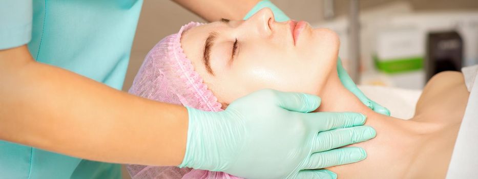 Cosmetologist with gloved hands applies a moisturizing mask with peeling cream on the female face. Facial cosmetology treatment. Procedures for facial care