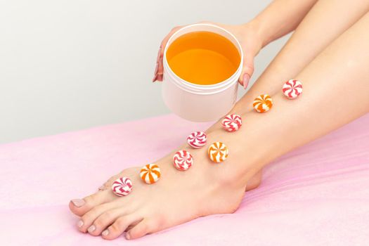 Depilation, waxing concept. Round candies lying down in a row on the female leg with a jar of sugar paste, close up