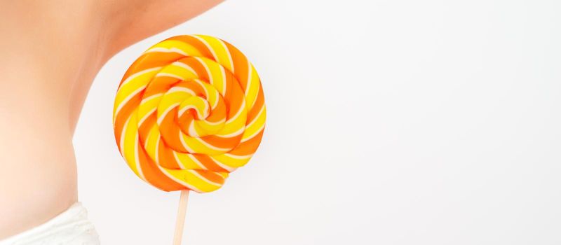 Waxing, depilation concept. A young female holds a round lollipop near her armpit on white background