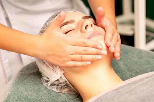 Facial treatment massage. Beautiful young caucasian woman with perfect skin receiving face and neck massage at a beauty spa