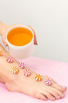 Depilation, waxing concept. Round candies lying down in a row on the female leg with a jar of sugar paste, close up