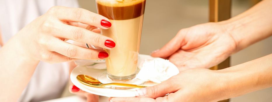 Barista serving coffee latte in glass mug for a customer, close up hands