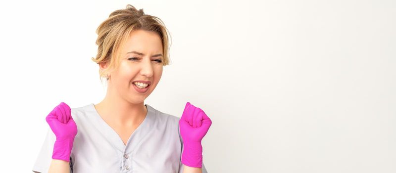 Happy caucasian woman doctor wearing pink gloves celebrates and raising fists on white background