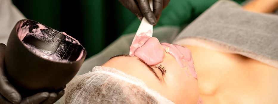 Beautiful young caucasian woman receiving an alginic mask to the face in beauty salon. Facial skin treatment