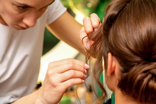 Hairstyling bride. A female hairdresser makes styling hair for the beautiful young caucasian woman in a beauty salon