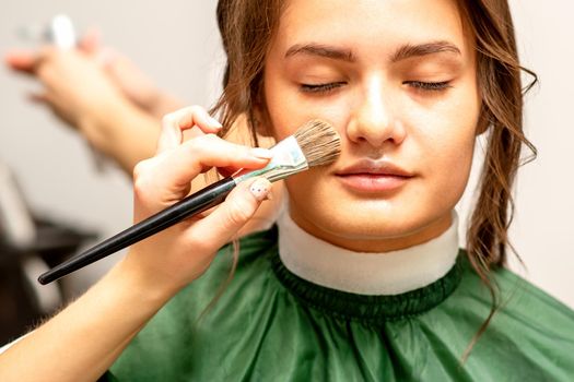 The makeup artist applies a cosmetic tonal foundation on the face using a makeup brush