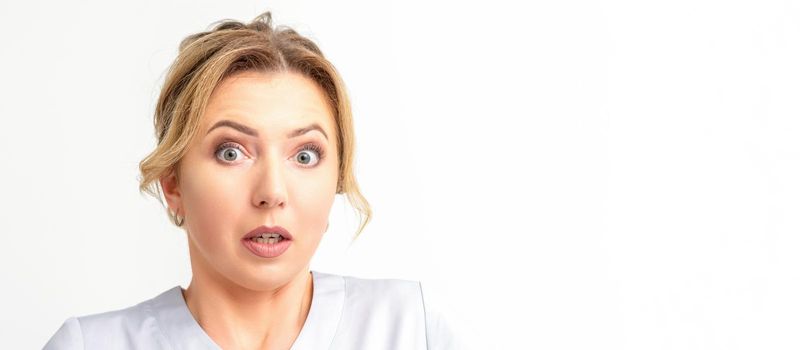 Female doctor shocked. Close up portrait of a young caucasian woman looking surprised with wide eyes stared isolated white wall background