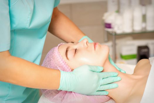 Cosmetologist with gloved hands applies a moisturizing mask with peeling cream on the female face. Facial cosmetology treatment. Procedures for facial care