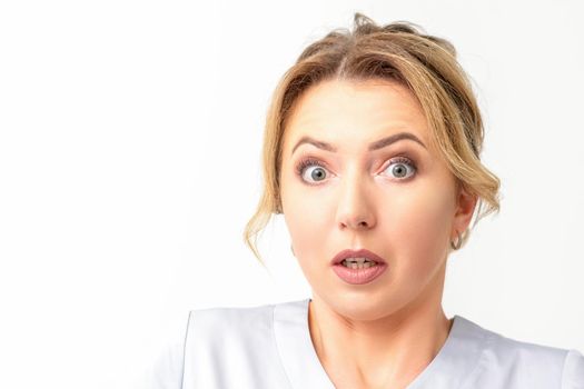 Female doctor shocked. Close up portrait of a young caucasian woman looking surprised with wide eyes stared isolated white wall background