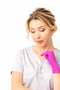 Young caucasian female doctor wearing gloves thoughtful looking down against a white background