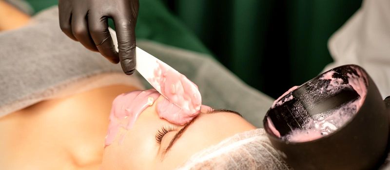 Beautiful young caucasian woman receiving an alginic mask to the face in beauty salon. Facial skin treatment