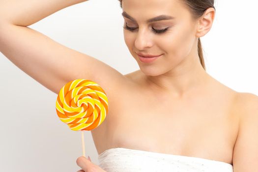 Waxing, depilation concept. The beautiful young caucasian woman covers her armpit with a lollipop on white background