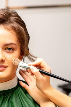 The makeup artist applies a cosmetic tonal foundation on the face using a makeup brush