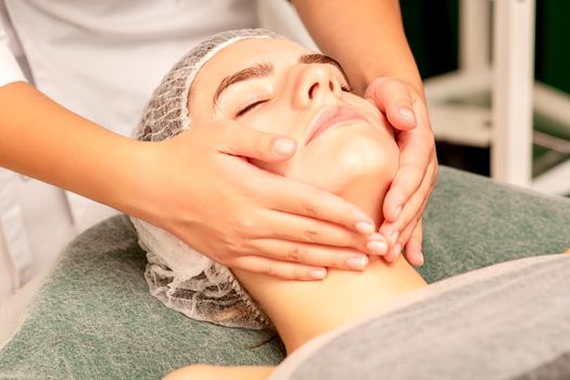 Facial treatment massage. Beautiful young caucasian woman with perfect skin receiving face and neck massage at a beauty spa