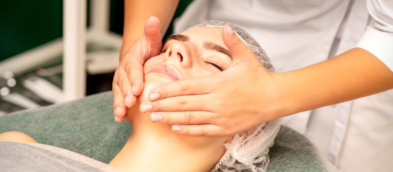 Facial treatment massage. Beautiful young caucasian woman with perfect skin receiving face and neck massage at a beauty spa