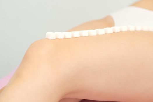 The concept of epilation, waxing. Sugar cubes lie down in a row on the naked white female leg
