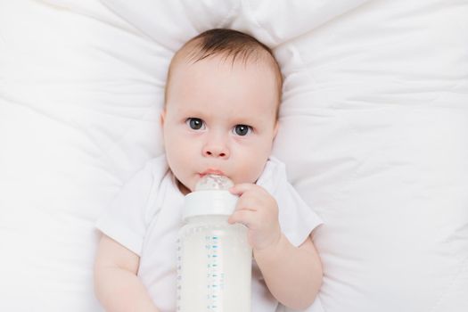 The baby in his crib eats from a bottle . Baby food copyspace . Artificial feeding. Kid top view