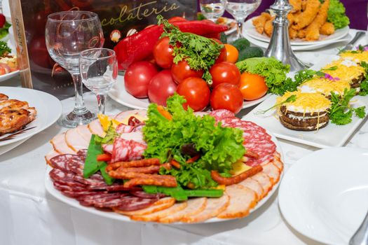 A plate of cold appetizers with various sausages, meat, and cheese. Greens and tomatoes.