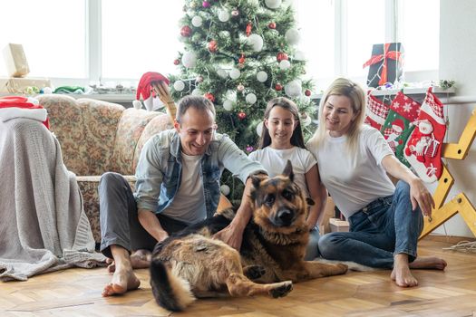 smiling family and daughter with dog sitting near christmas tree with gifts.