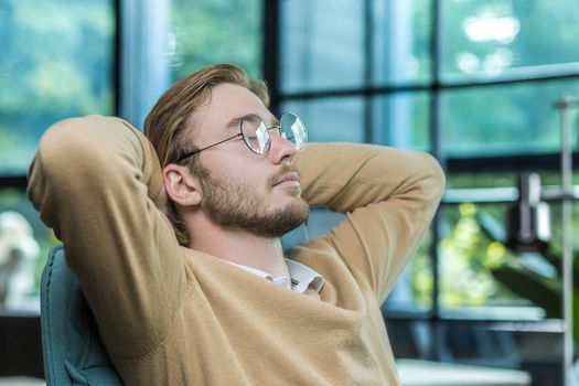 A close-up photo of a man resting in the office, a businessman with his hands behind his head with his eyes closed is dreaming, a close-up photo