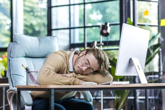 Young businessman resting in office, man in glasses sleeping on table, freelancer using computer, daytime sleep