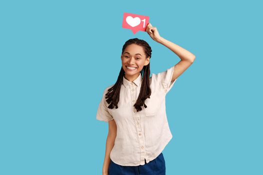 Social media Like button. Woman with black dreadlocks posing with pleasant smile, recommending to follow and share blog with trendy content. Indoor studio shot isolated on blue background.