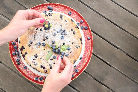 a woman's hand decorates a fresh pie with blueberries, bucking at home, exotic food, delicious dessert. High quality photo