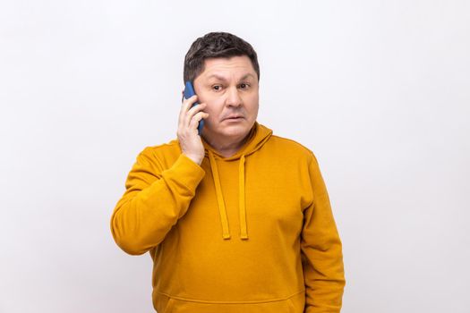 Serious man standing, talking smartphone, making call and having important conversation with friend or business partner, wearing urban style hoodie. Indoor studio shot isolated on white background.