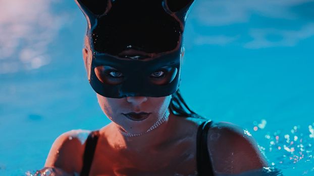 Sexy woman in bunny latex mask swimming in pool at night. Attractive chick in black swimsuit enjoying party time. Rich lifestyle, luxury life, entertainment, masquerade. Dangerous girl. High quality