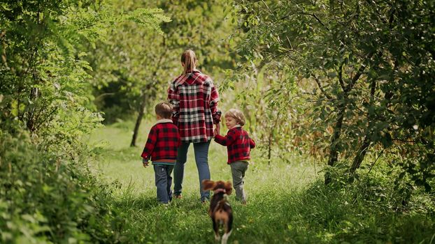Young family - mom and two brothers twins boys runs with puppy beagle dog in green park or garden. Happy mother and children, love, freedom, future concept. High quality photo