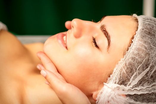 Facial massage. Hands of a masseur massaging neck of a young caucasian woman in a spa salon, the concept of health massage