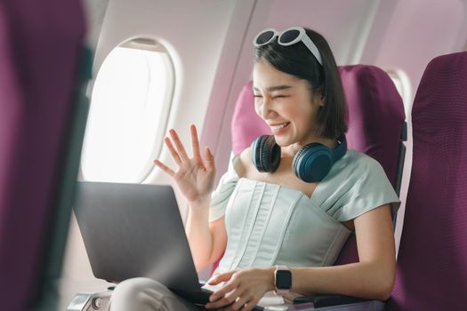 Joyful asian woman sits in the airplane and using laptop while go to travel.