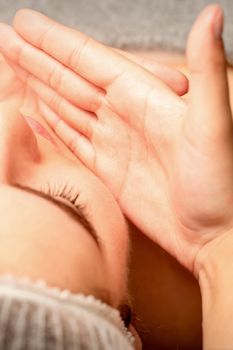 Beautiful caucasian young woman receiving a facial massage with closed eyes in spa salon, close up. Relaxing treatment concept