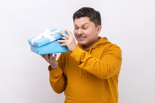 Portrait of middle aged man opening gift box and peeping inside with frowning face, unpleasant surprise, wearing urban style hoodie. Indoor studio shot isolated on white background.