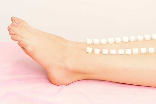 The concept of epilation, waxing. Sugar cubes lie down in a row on the naked white female leg