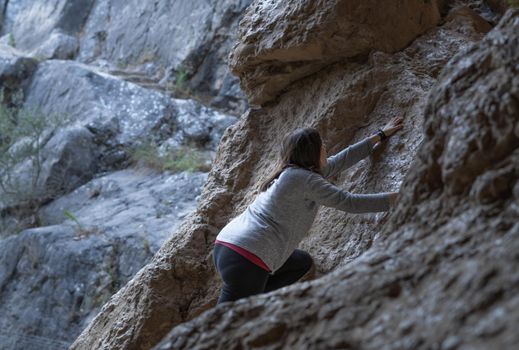 young girl learning rock climbing in high mountain with blue sweater, black tights and boots.