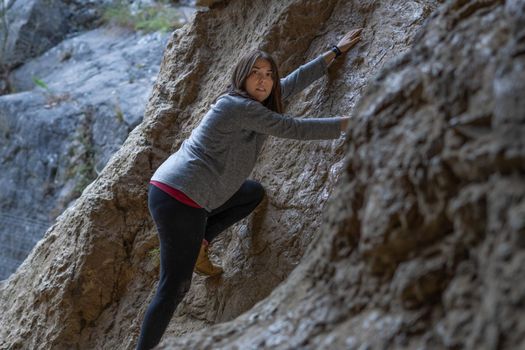 young girl learning rock climbing in high mountain with blue sweater, black tights and boots.