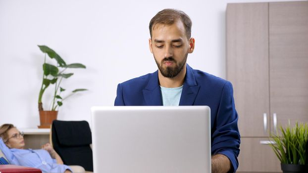 Freelancer businessman working on the laptop computer in the house and his wife is in the background