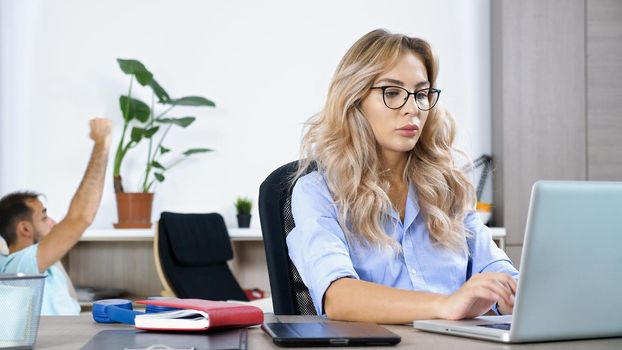 Freelancer woman working on the computer laptop in the house while the husband is watching TV in the background