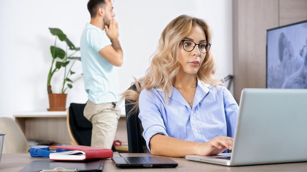 Freelancer woman working on the computer laptop in the house while the husband is watching TV in the background