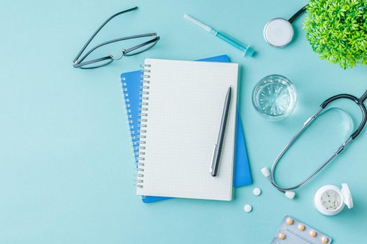 Medical equipment with stethoscope and spiral notebook in doctor office on green desk background top view. Nurse desktop concept.