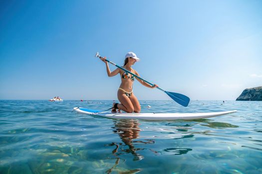 young woman in swimsuits doing yoga on sup board in calm sea, early morning. Balanced pose - concept of healthy life and natural balance between body and mental development