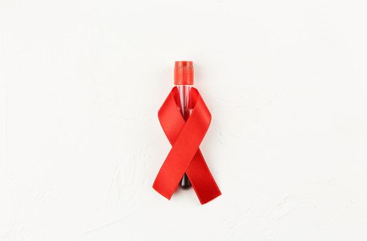 Red ribbon with vacutainer on a white grunge background. Top view. Health care. AIDS prevention concept. Hiv and cancer awareness. Test tube container. Flat lay.