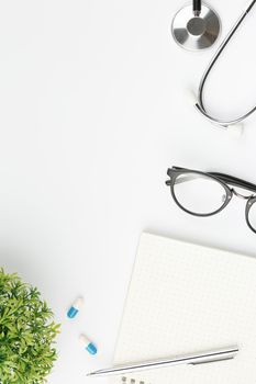 Open spiral notebook with pen and glasses flat lay. Stethoscope with medical mask and pills on white isolated background top view. Doctor's desktop concept.