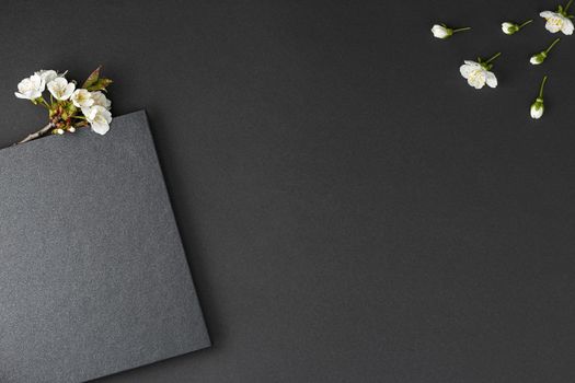 Black notebook with white cherry flowers on dark isolated background flat lay.