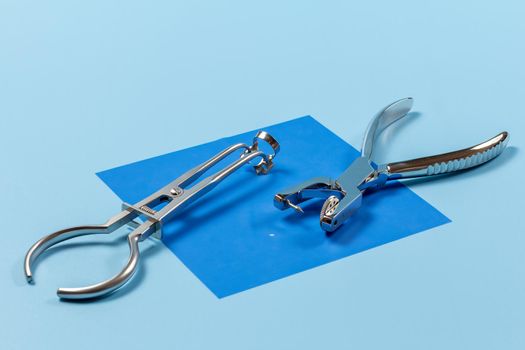Dental hole punch and a rubber dam forceps with the clamp on the blue rubber dam. Medical tools concept.