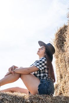 Beautiful girl on straw bales. beautiful woman in plaid shirt and cowboy hat resting on haystack