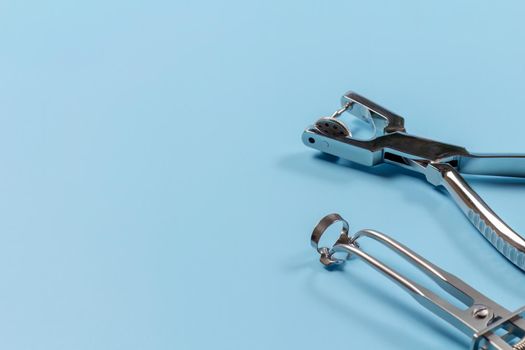Dental hole punch, the rubber dam forceps and the clamp on the blue background. Medical tools concept.